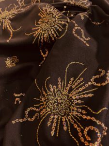 Providan, lagan materijal u braonkastoj nijansi, nalik muslinu ili žoržetu, sa blagom elastičnošću i raskošnim zlatnim šarama prošaranim šljokicama koje svetlucaju poput kiše svetlosti.