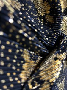 Plisirana likra - Luxe Dust je elastičan i neprovidan materijal sa plisiranom teksturom i raskošnim zlatnim printom na crnoj podlozi.