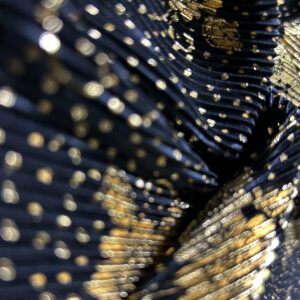 Plisirana likra - Luxe Dust je elastičan i neprovidan materijal sa plisiranom teksturom i raskošnim zlatnim printom na crnoj podlozi.